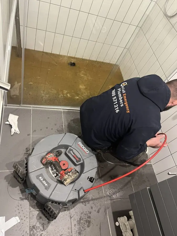 Plumber clearing a bathroom floor drain, Chelsea