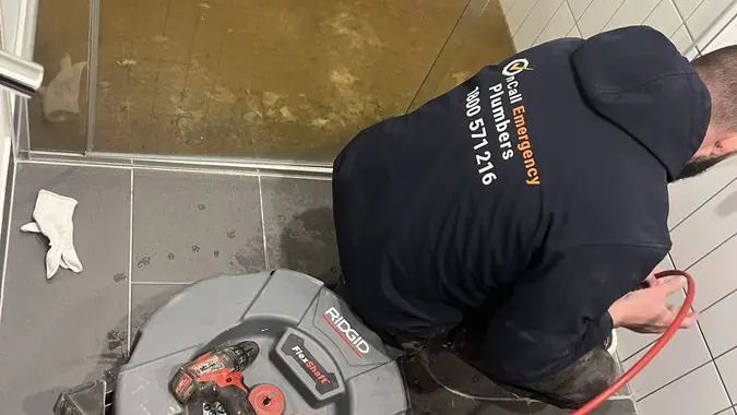 Plumber clearing a bathroom floor drain, Chelsea